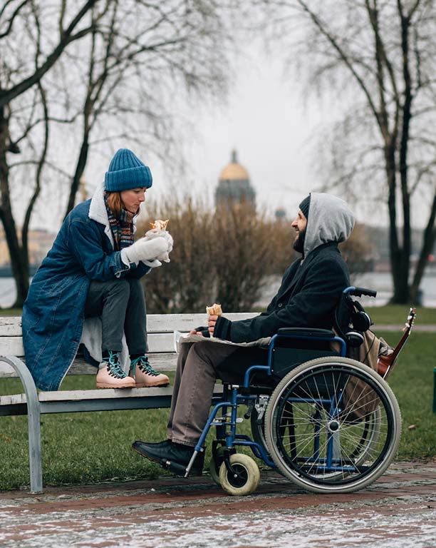 Mann im Rollstuhl und Frau sitzt auf Bank
